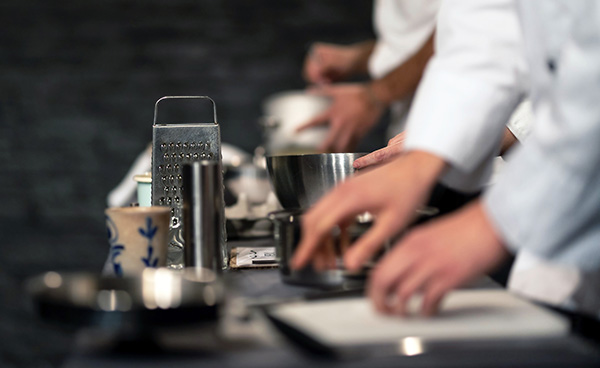 Team of professional chefs preparing food in a commercial kitchen. Cooks in the production process of system catering. An inside view of a pro catering kitchen in Spain. Extreme narrow depth of field.